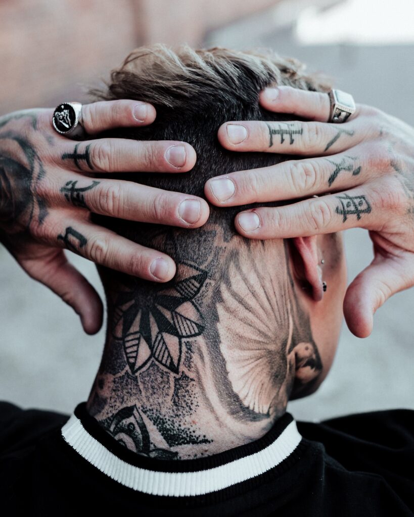 Man with tattoos all over neck and and fingers. This picture is used as it contrasts the human body naturally and with alterations. 